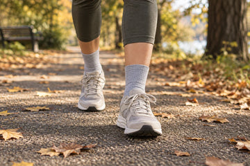 Walker wearing light grey crew socks and neutral sneakers on an autumn park path; illustrative scene, not MP product photography